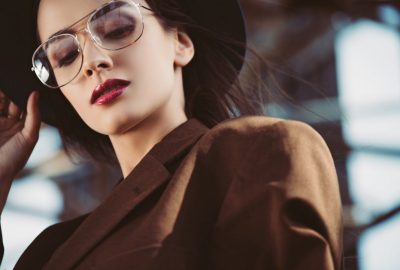 elegant-young-woman-posing-in-hat-eyeglasses-and-brown-jacket-on-roof.jpg